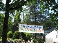 Banner über einer Menschengruppe, Text: Kirchweihfest Pfingstmontag ab 11 Uhr, Gemeindezentrum St. Johannes im Hintergrund