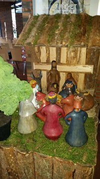 aus bunt bemalten Ton gestaltete Krippenfiguren vor einem hölzernen Stall, die heiligen drei Könige knieen vor der Krippe, ein Grünkohlblatt