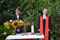 Konfirmand Tjark Sievers und Pfarrerin Ulrike Klank hinter einem Altartisch im Garten