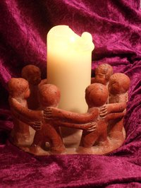 Freundeskreis: Tonfiguren, die mit den Händen auf der Schulter des Nachbarn einen Kreis bilden, brennende Kerze in der Mitte