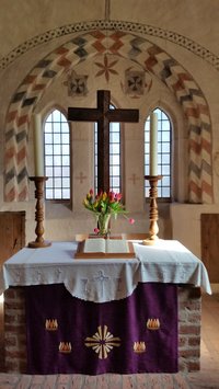 Altar der St. KAtharinenkirche, aufgeschlagene Bibel, Kreuz, Tulpenstrauß und Kerzen auf Leuchtern, Architektur begleitende Ausmalung um die Fenster, lila Altarbehang