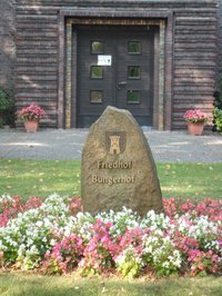 Blöick auf das Tor der Friedhofskapelle des städtischen Friedhofs Bungerhof, davon ein Findling mit Inschrift Friedhof Bungerhof