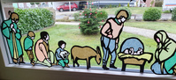 Fensterbild Krippe: Maria und Joseph an der Krippe mit dem Jesuskind, Esel und Hirten, teilweise auf Knien im Hintergrund kleiner Tannenbaum mit roten Kugeln, rotes Auto auf der anderen Straßenseite 