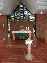 Altartisch vor den Buntglasfenstern im St. Johanneshaus mit dem Taufschalenständer im Vordergrund