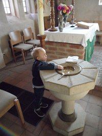 Dreiojähriger am Taufstein in St. Katharinen Schönemoor, die Hand in das Taufbecken ausstreckend