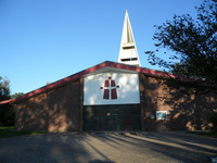 Gotteshaus der Christengemeinde Delmenhorst e.V. in Annenheide, Christusfigur in rot auf weißem Feld am Giebel, spitzer Turm
