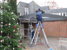 Handwerker errichten vor dem Eingang zum Johannes Haus den Rahmen für ein Glasdach - am linken Bildrarnd ist der geschmückte Weihnachtsbaum zu erkennen.