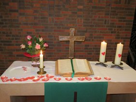 Altar im St. Johannes Haus mit Blumen und Kerzen und gestalteten Herzen aus rotem Karton mit je einem Teelicht