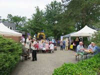 Zeltpavillons vor dem St. Johannes Haus mit Angeboten zum Essen, stehende und sitzende Menschen, eine gelbe Hüpfburg im Hintergrund