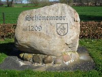 großer Findling auf Feldsteinfundament mit dem Schriftzug Schönemoor seit 1209 und dem Wappen der alten Kommune Schönemoor: ein Sämann
