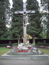 großes Kreuz auf gestuftem Sockel mit zahlreichen Grablichtern und Engelfiguren