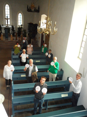 Pfarrerinnen und Pfarrer aus Delmenhorst und Stuhr stehen in der Laurentiuskirche Hasbergen und halten Schilder mit Schwerpunktaufgaben in die Höhe 