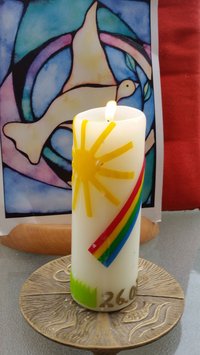 dircke Kerze mit Sonnensymbol und Regenbogen auf Bronzeteller mit Fisch