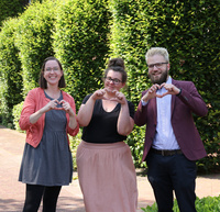 Tabina Bremicker, Svenja Lange und Christoph Martsch-Grunau zeigen mit den Fingern das Herz-Zeichen: wir lieben unsere Aufgabe