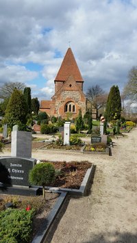 Grabreihe mit verschiedenen  Grabmalen, die Kirche vor einem blauen Himmmel mit Wolken 