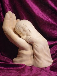 Skulptur einer Hand, in die sich eine menschliche Figur hinein schmiegt, vor lila Tuch 