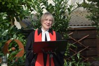 Pfarrerin Ulrike Klank im schwarzen Talar mit roter Stola am Redepult im Garten bei einer Konfirmationsfeier
